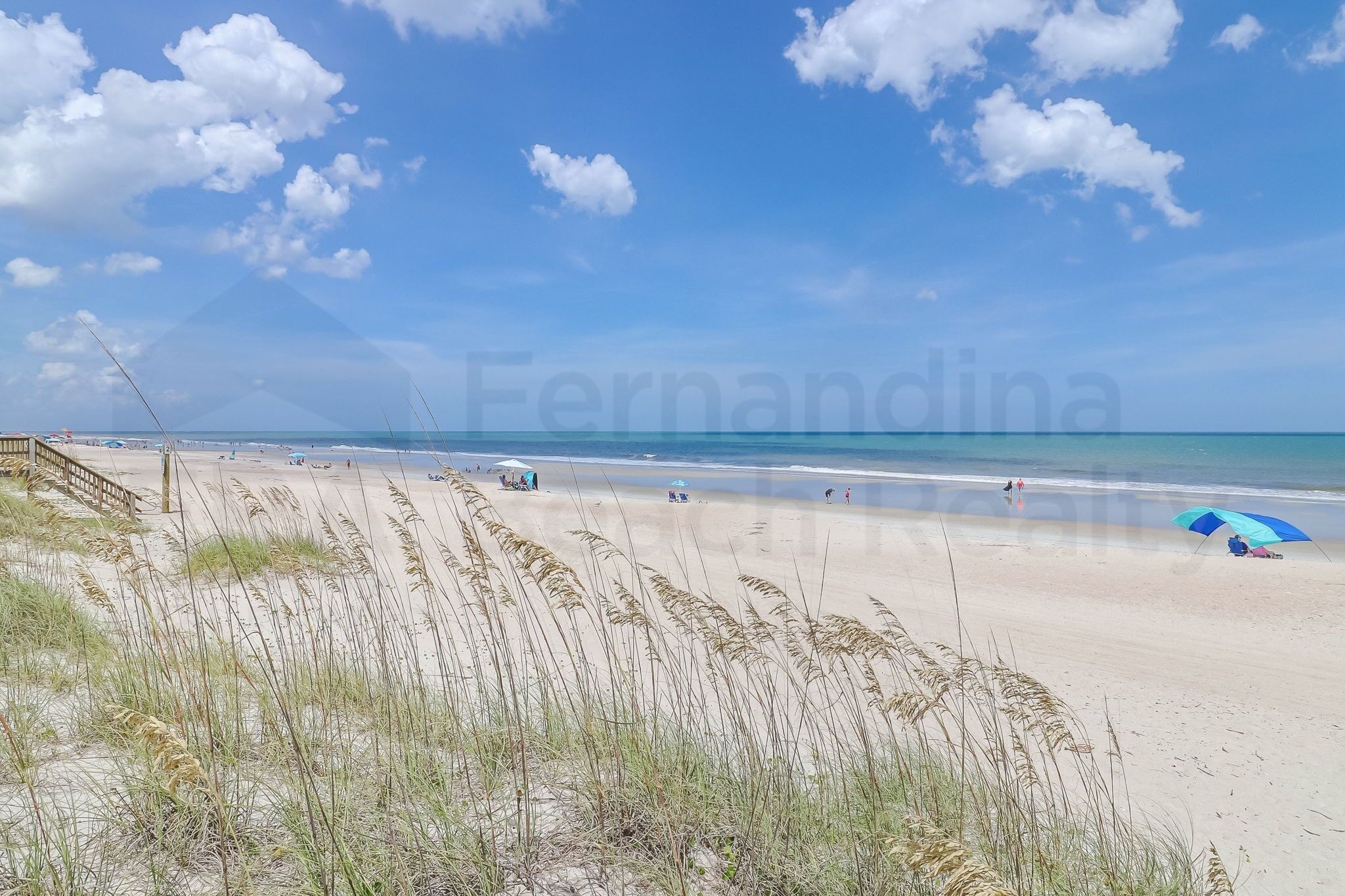A beach with a wooden walkway, beachgoers, and a clear sky.