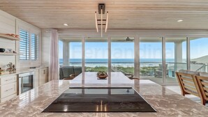 A modern kitchen with a large island, a dining area with a view, and a balcony with a railing.