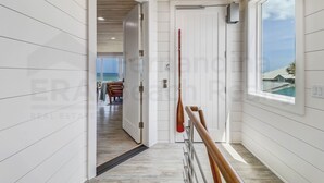A hallway with white paneled walls, a wooden ceiling, and a view of the ocean through a window.