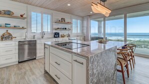 A modern kitchen with white cabinetry, a marble island, and a view of the ocean.