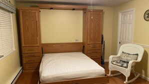 Een slaapkamer met een houten bedframe, een witte matras, een schommelstoel en een plafondventilator.