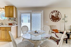A dining area with a glass table, white chairs, and a plaid chair with an orange cushion. A decorative sign on the wall reads "GONE FISHING." - 534 N. Fletcher Ave. #1 2 Bedroom Cottage by RedAwning (Fernandina Beach)