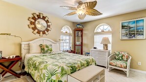 A bedroom with a bed, a ceiling fan, a fish wall art, a chair, and a window with blinds. - 534 N. Fletcher Ave. #1 2 Bedroom Cottage by RedAwning (Fernandina Beach)