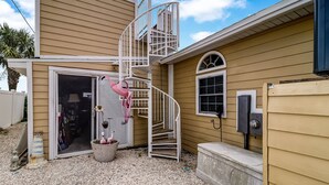 A house with a spiral staircase, a door with a pink flamingo decoration, and a small garden area with pebbles. - 534 N. Fletcher Ave. #1 2 Bedroom Cottage by RedAwning (Fernandina Beach)