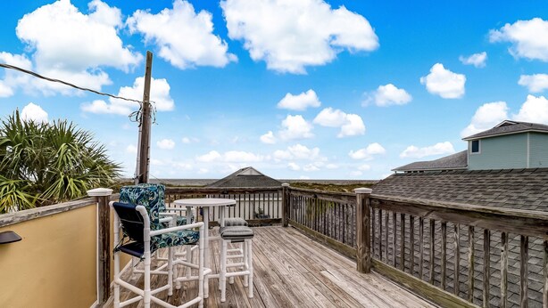 A wooden deck with outdoor furniture, a railing, and a view of the sky and clouds. - 534 N. Fletcher Ave. #1 2 Bedroom Cottage by RedAwning (Fernandina Beach)