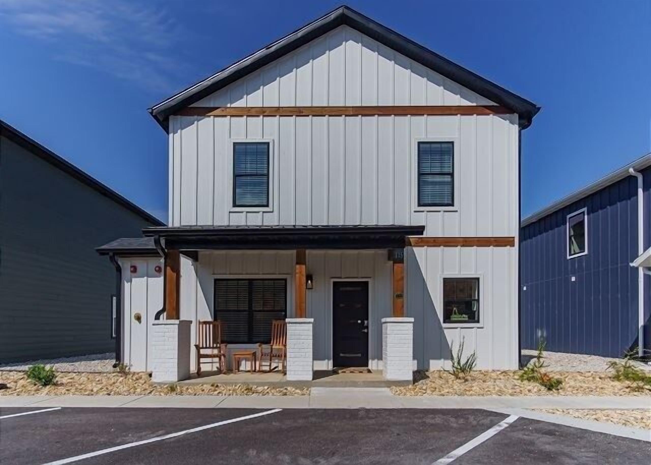 A two-story building with a front porch, a black door, and a small patio area with chairs.
