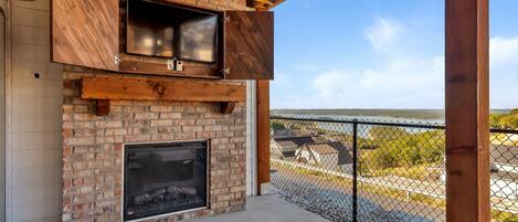 An outdoor patio with a brick fireplace, a flat-screen TV, and a cushioned seating area.