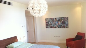 Une chambre à coucher avec un lit, un fauteuil rouge, une porte blanche et un mur orné d’un collage de couvertures de magazines.