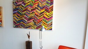 A red leather armchair in a room with a colorful abstract painting on the wall and a tall floor lamp. - One Woodbrook Place convenient condo with a city view  (Port of Spain)