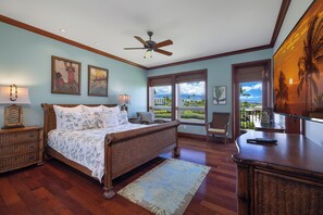 A bedroom with a large bed, a ceiling fan, and a view of the ocean through the windows.