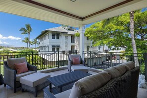 A covered outdoor seating area with wicker furniture and a view of a white building.