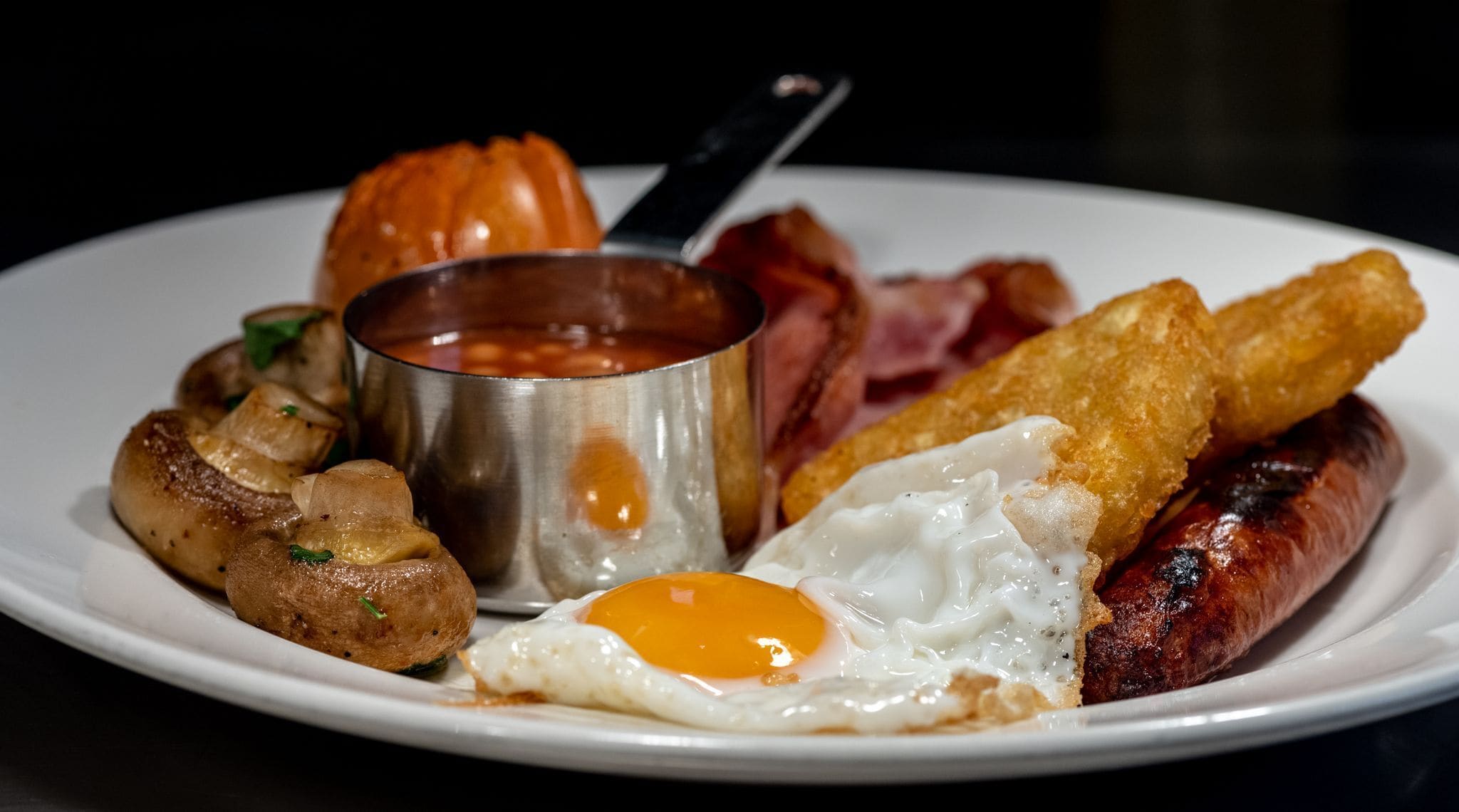 Un plato de comida para el desayuno con salchichas, huevos, tocino, champiñones y tostadas.
