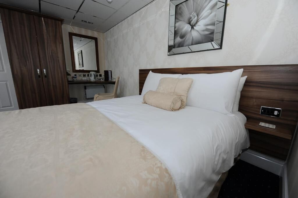 A hotel room with a large bed, a wooden headboard, a bedside table, a mirror, and a wall-mounted artwork.
