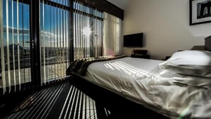 Een hotelkamer met een bed, een televisie en een groot raam met jaloezieën.