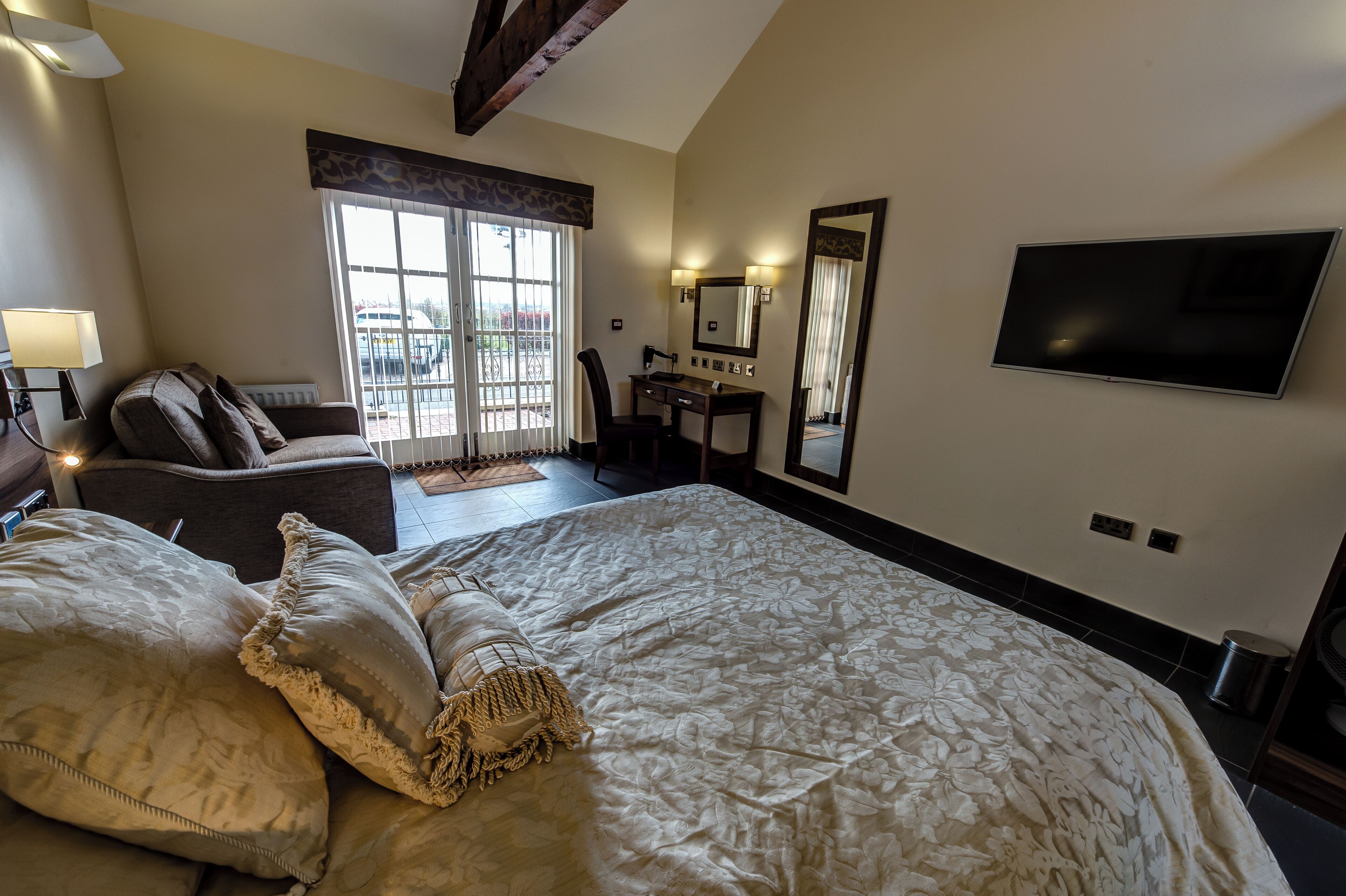 A hotel room with a large bed, a desk, a chair, a TV, and a view of the outside.