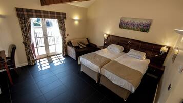 A hotel room with two beds, a sofa, a desk, and a window with curtains.