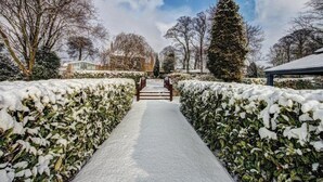 Een sneeuwbedekte pad, langs de randen omzoomd door heggen, leidt naar een gebouw met een glazen gevel.