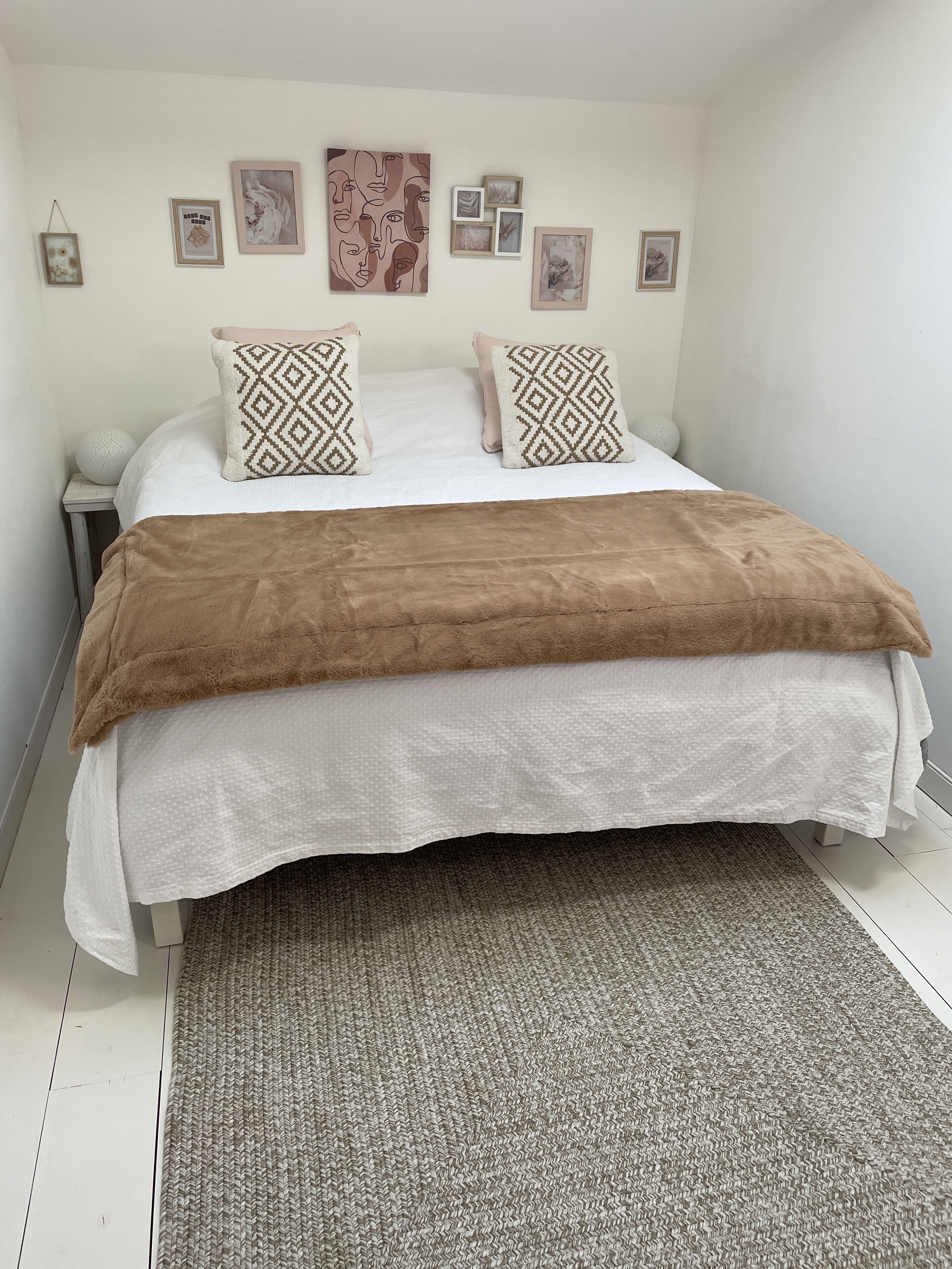 A bedroom with a bed, pillows, a rug, and wall art.
