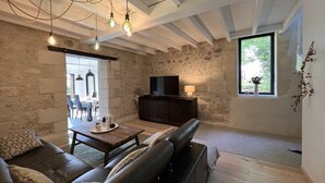 A cozy living room with a stone wall, a leather sofa, a wooden coffee table, and a television on a dark wooden cabinet. - Le Petit Chai Fronsadais - Gite *** 5 persons (Saint-Michel-de-Fronsac)