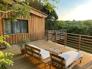 Eine Holzterrasse mit einer Bank und einem Tisch, mit Blick auf eine üppige, grüne Landschaft.