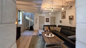 A modern living room with a wooden floor, a black leather sofa, a wooden coffee table, and a spiral staircase leading to an upper level. - Le Petit Chai Fronsadais - Gite *** 5 persons (Saint-Michel-de-Fronsac)