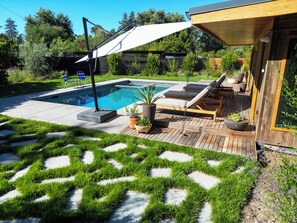 A backyard with a swimming pool, sun loungers, and a wooden deck.