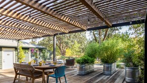 Um deck de madeira com pérgola, mobiliário de exterior e plantas em vasos.