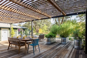 Eine Holzterrasse mit einem überdachten Pergola, Gartenmöbeln und Blumentöpfen.