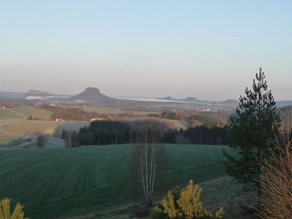 A panoramic view of a rural landscape with rolling hills, a prominent hilltop structure, and sparse tree coverage.