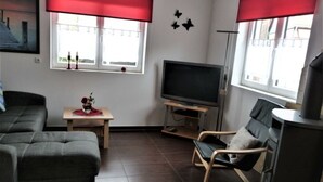 Un salon moderne avec un canapé, un téléviseur posé sur un meuble, une petite table avec un vase et une cheminée.