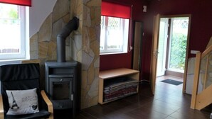 Un salon avec une cheminée en pierre, un fauteuil noir avec un coussin, un banc en bois et une porte donnant sur l’extérieur.