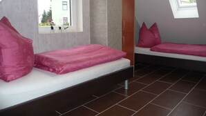 Une chambre de taille modeste, avec deux lits, une fenêtre et une vue sur l’extérieur.