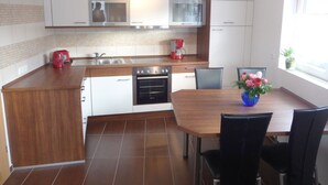 Une cuisine moderne avec des meubles blancs, un plan de travail en bois, un four encastré et un coin repas comprenant une table et des chaises.
