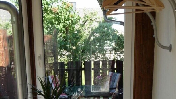 Une pièce avec une grande fenêtre, une plante en pot, un radiateur en métal et un cintre en bois.