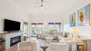A spacious living room with a fireplace, comfortable seating, a flat-screen TV, and artwork on the walls.