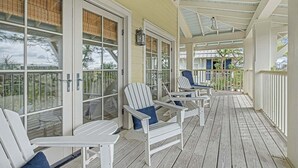 A covered porch with white Adirondack chairs and a wooden deck.
