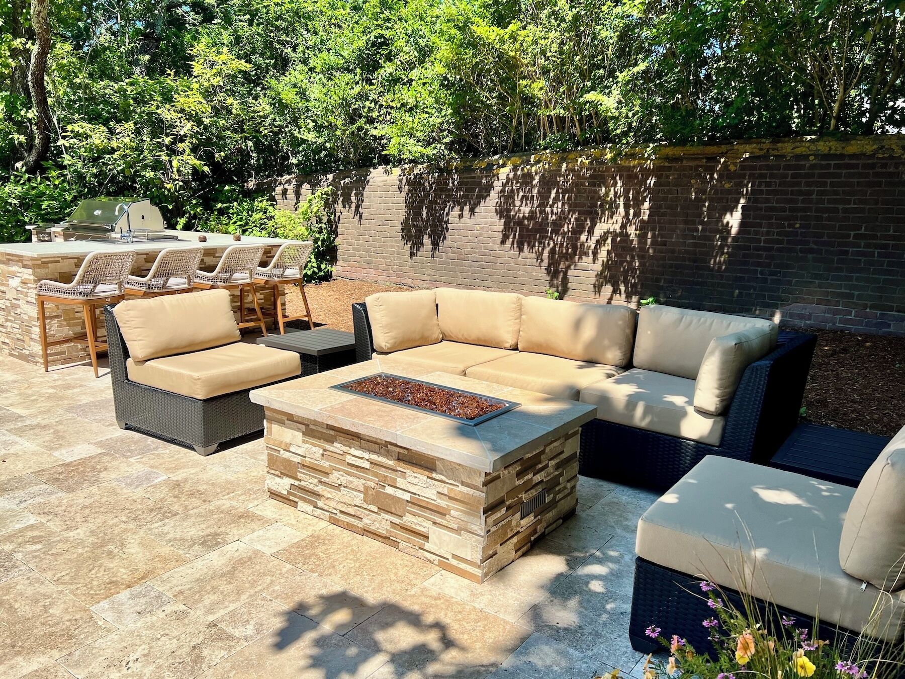 An outdoor patio with a stone fire table, cushioned seating, and a brick wall backdrop.