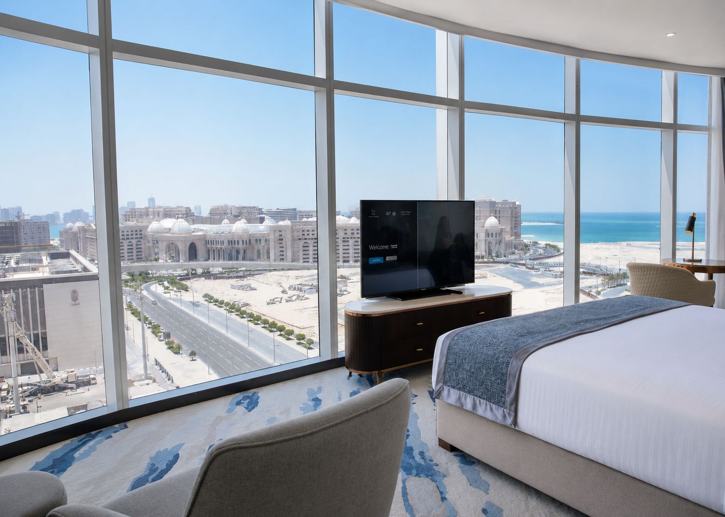 Una camera d'albergo con una grande finestra, un letto, una TV e vista sulla città e sulla spiaggia.