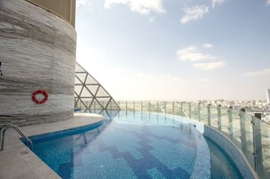 Una piscina infinita moderna con barandilla de vidrio, un flotador salvavidas y vistas a la ciudad.
