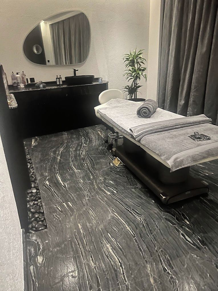 Een moderne badkamer met een vloer van zwart marmer, een zwart bad, een witte bank, een ronde spiegel en een plant in pot.