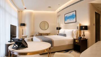 Habitación de hotel con cama, mesitas de noche, escritorio, silla, televisor y una ventana grande.