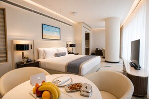 Habitación de hotel con cama, mesitas de noche, escritorio, silla, televisor y frutero.