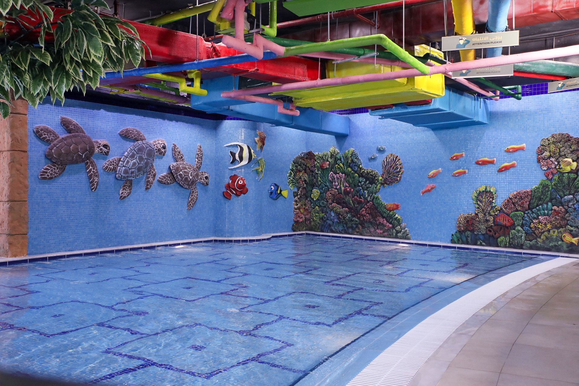 Une piscine intérieure ornée d’une fresque représentant des créatures marines et d’un panneau de signalisation de sécurité.