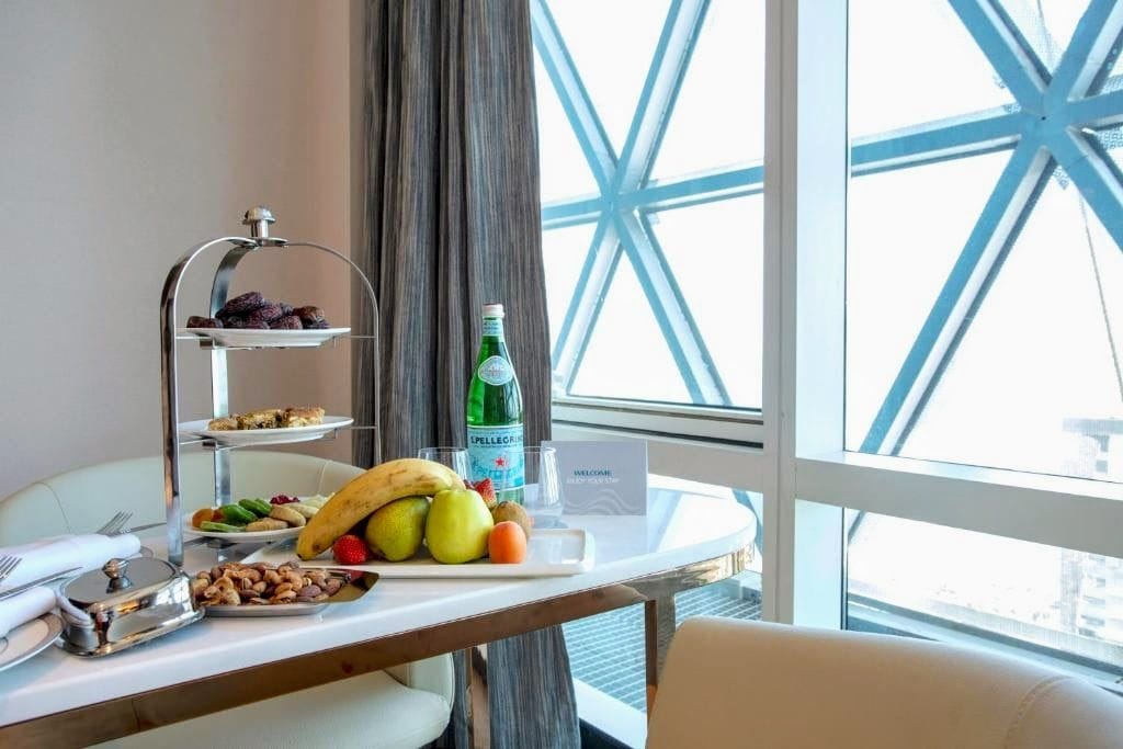 A breakfast setup with a fruit bowl, a bottle of Pellegrino water, and a sign reading 'Welcome.'