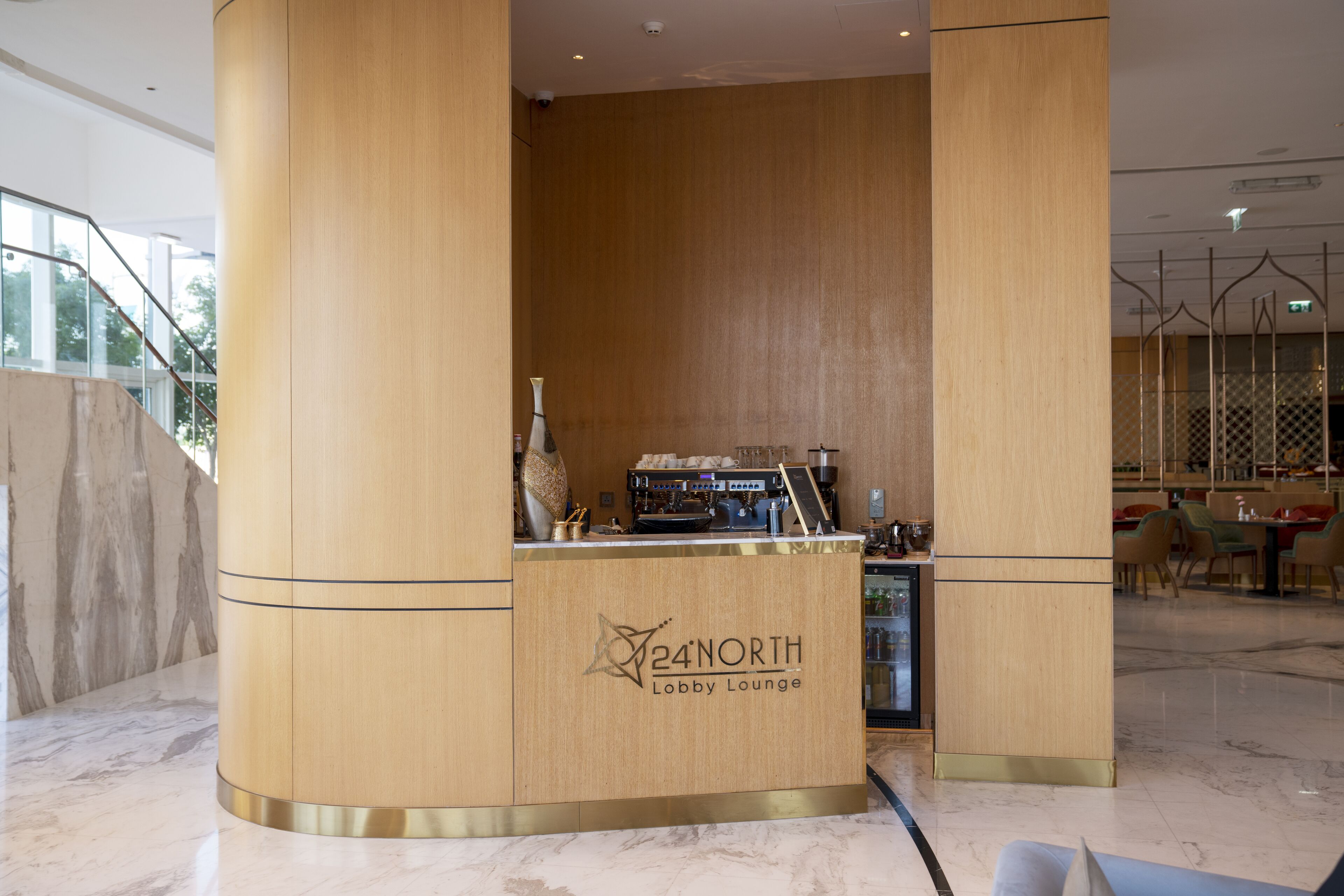 A lobby lounge with a wooden reception desk, a coffee machine, and seating area.