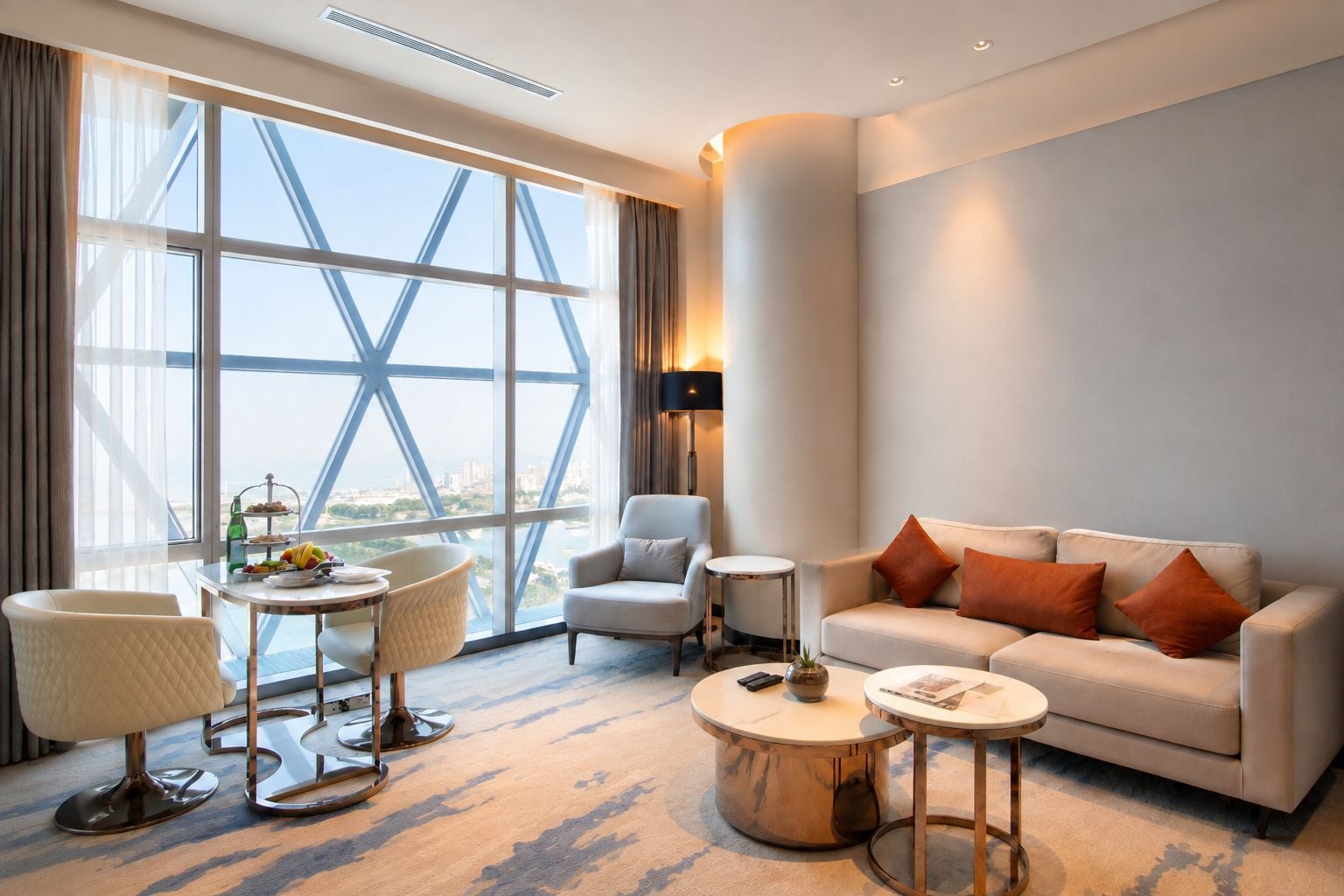 Una habitación de hotel moderna con un ventanal grande, un sofá, una mesa redonda de centro y una silla.