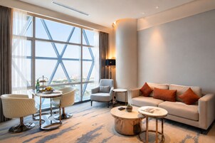 Una habitación de hotel moderna con un ventanal grande, un sofá, una mesa redonda de centro y una silla.