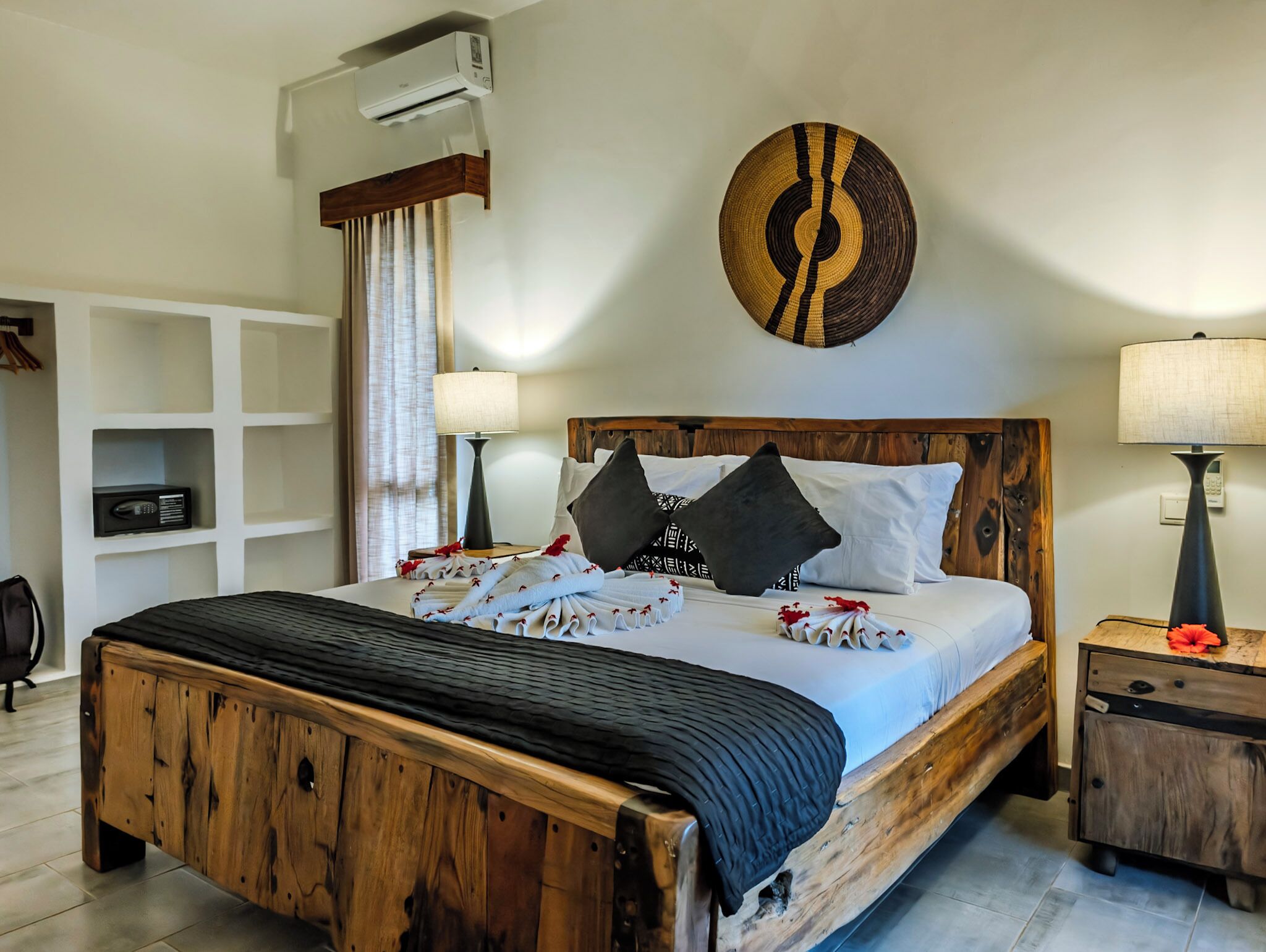 A wooden bed with a headboard, a bedside table, a lamp, and a wall-mounted air conditioner.
