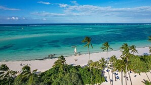 A beach with clear turquoise water, palm trees, and a sandy shore. - Tamu Tamu Boutique Hotel (Pwani Mchangani)