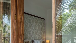A bedroom with a bed, pillows, a nightstand, and a view of palm trees through a glass door. - Tamu Tamu Boutique Hotel (Pwani Mchangani)